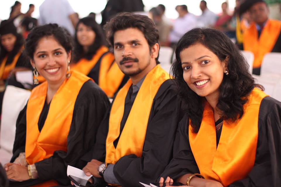 Two women and a man seated wearing black and yellow robes that's traditionally worn for convocation. All three looking into the camera smiling. 